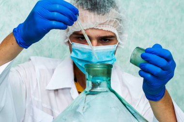 Beyaz önlüklü bir laboratuvar asistanı koruyucu maske, eldivenler ve laboratuardaki bir kapak pipetli bir damara sıvı damlatıyor, doktorun yüzü bulanık. Yüksek kalite fotoğraf