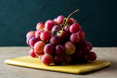 Karanlık bir arka planda, kesme tahtasındaki pembe üzümlerden oluşan bir masa fırçası. Yüksek kalite fotoğraf