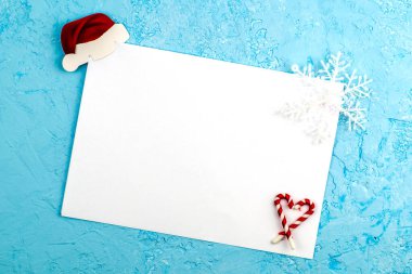 Çarşafın üst köşesinde mavi bir yüzey üzerinde beyaz bir çarşaf var. Kağıt bir Noel Baba şapkası ve bir kar tanesi var. Alt köşede kalp şeklinde katlanmış şekerler var. Yüksek kalite fotoğraf