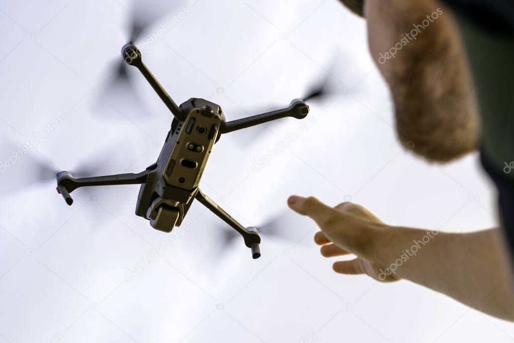 a tourist guy in a hat launches a quadcopter into the sky and reaches for it with his hand. High quality photo
