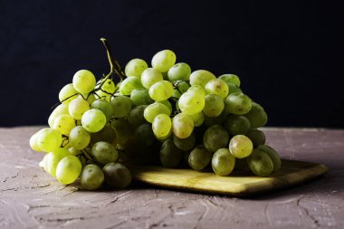 Karanlık bir arka planda kesme tahtasındaki beyaz üzümlerden oluşan bir masa fırçası. Yüksek kalite fotoğraf