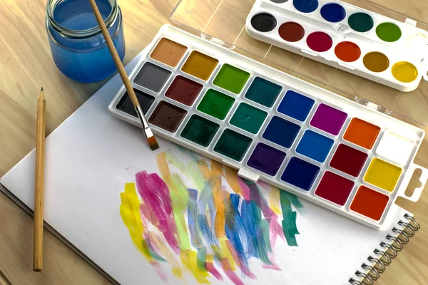 watercolor paints brush jar of water on a white sheet with samples of paints. High quality photo