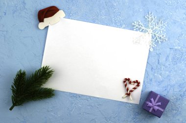 Yeşil köknar dalları, hediye kutuları ve kar taneleriyle çerçevelenmiş mavi bir yüzey üzerinde beyaz bir çarşaf Noel Baba 'ya yeni yıl dilekleriyle yazılmış kavramsal bir mektup. Yüksek kalite fotoğraf