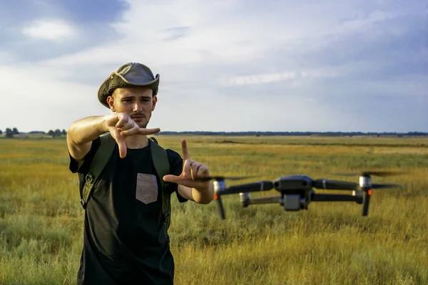 a young tourist guy in a hat shoots landscapes of the area on a quadcopter holding a frame made of fingers in front of him. High quality photo