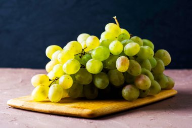 Karanlık bir arka planda kesme tahtasındaki beyaz üzümlerden oluşan bir masa fırçası. Yüksek kalite fotoğraf