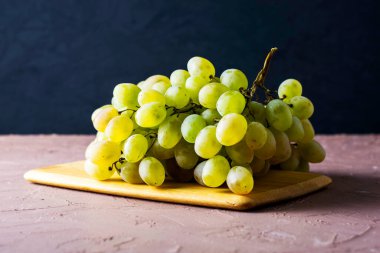 Karanlık bir arka planda kesme tahtasındaki beyaz üzümlerden oluşan bir masa fırçası. Yüksek kalite fotoğraf