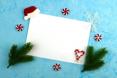 Mavi bir yüzeyde beyaz bir yaprak, yeşil köknar dallarıyla çerçevelenmiş, lolipoplar ve kar taneleriyle - Noel Baba 'ya yeni yıl dilekleriyle yazılmış kavramsal bir mektup. Yüksek kalite fotoğraf