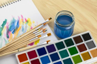 Suluboya, boya örnekleriyle dolu beyaz bir çarşaf üzerinde fırça dolu su kavanozunu boyar. Yüksek kalite fotoğraf