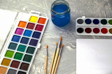 Suluboya boya, gri bir yüzey üzerinde bir kavanoz su ve beyaz kağıt fırçalar. Yüksek kalite fotoğraf