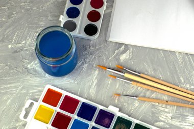 Suluboya boya, gri bir yüzey üzerinde bir kavanoz su ve beyaz kağıt fırçalar. Yüksek kalite fotoğraf