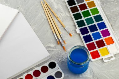 Suluboya boya, gri bir yüzey üzerinde bir kavanoz su ve beyaz kağıt fırçalar. Yüksek kalite fotoğraf