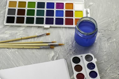 Suluboya boya, gri bir yüzey üzerinde bir kavanoz su ve beyaz kağıt fırçalar. Yüksek kalite fotoğraf