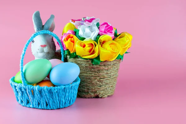 Easter bunny and painted Easter eggs in a basket next to a basket of flowers on a pink background. copyscape — Stock Photo, Image
