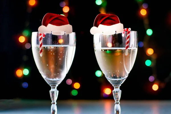 Två glas champagne med dekoration i form av en jultomte hatt, karamell godis på en svart bakgrund med bakgrundsbelysning närbild — Stockfoto