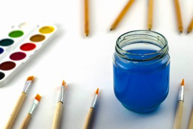 Suluboya, beyaz bir arka plan üzerinde bir kavanoz su ve kalem fırçalar. Yüksek kalite fotoğraf