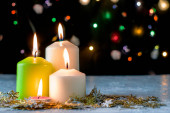 černé vánoční pozadí s barevnými světly hořící svíčky a dekorativní sněhové vločky v popředí. Kvalitní fotografie