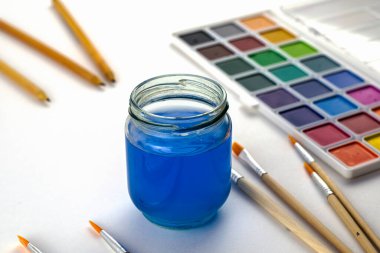 Suluboya, beyaz bir arka plan üzerinde bir kavanoz su ve kalem fırçalar. Yüksek kalite fotoğraf