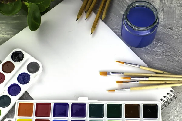 Suluboya kalemleri, beyaz bir kağıt tabakasını ve gri arka planda bir bitkiyi boyar. Yüksek kalite fotoğraf