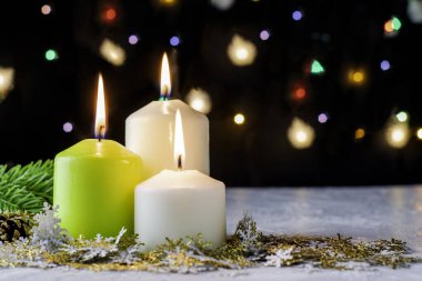 Siyah Noel arka planında renkli ışıklar yanan mumlar ve ön planda dekoratif kar taneleri var.