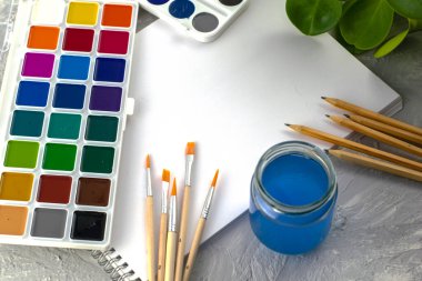 suluboya kalemler fırçalar beyaz bir sayfa kağıt ve gri arka planda bir bitki