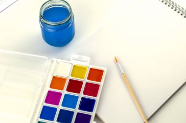 Suluboya, bir kavanoz su ve beyaz bir yüzeye çizim için bir çizim defteri çizmek için bir fırça boyar. Yüksek kalite fotoğraf