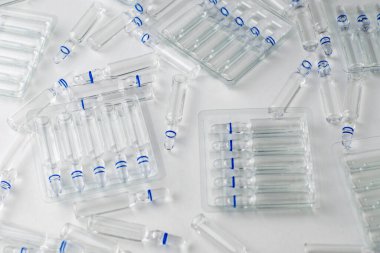 Beyaz zemin üzerinde cam ampulleri ve ayrı ampulleri olan şeffaf plastik kaplar.