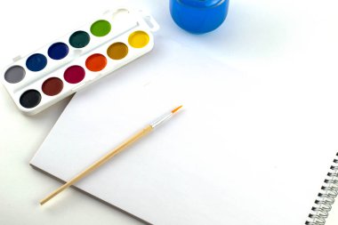 Suluboya fırça kavanozunu suyla boyar ve eskiz defterini beyaz arka planda tutar. Yüksek kalite fotoğraf