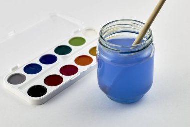 Beyaz arka planda suluboya boyalar ve bir kavanoz su içinde boya fırçası. Yüksek kalite fotoğraf