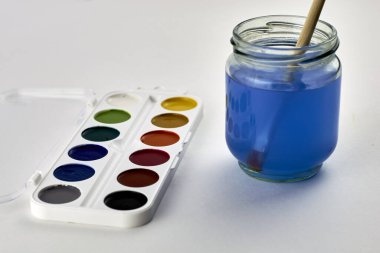 Beyaz arka planda suluboya boyalar ve bir kavanoz su içinde boya fırçası. Yüksek kalite fotoğraf