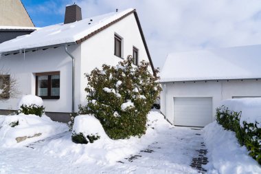 Su oluğunda buz saçakları olan karla kaplı ev ve garaj
