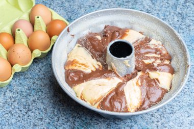 A bundt pan with a fresh dough for marble cake and eggs beside