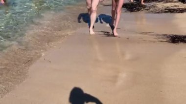 Deniz kenarında kumlu bir plajın kıyısında yürüyen ayaklar. Oğul ve baba