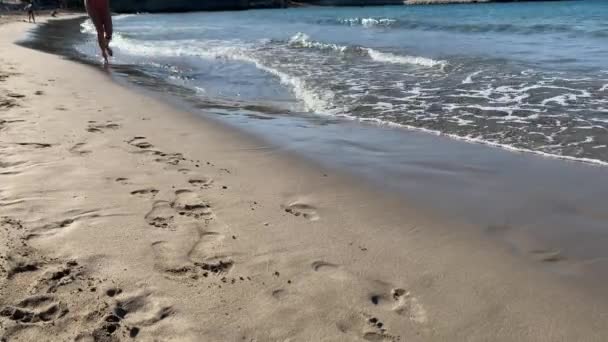 Slanke vrouwelijke poten en voeten die langs zeewatergolven op zandstrand lopen. Mooie vrouw wandelt op zee surf. plons van water en schuim meisje na het baden in de oceaan gaan aan wal. — Stockvideo