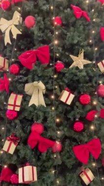 Alışveriş merkezindeki Noel ağacı. Şenlikli yeşil yapay Noel ağacı oyuncaklar, altın toplar, çelenkler ve hediyelerle süslenmiş. Tepeden tırnağa hareket ediyor. Yeni yıl tatili kavramı