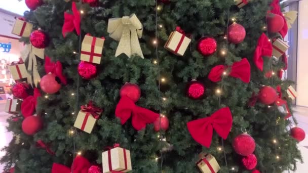 Árbol de Navidad en el centro comercial. Árbol de Navidad artificial verde decorado con juguetes, bolas de oro, guirnaldas, regalos. Movimiento de abajo hacia arriba. El concepto de vacaciones de Año Nuevo — Vídeo de stock