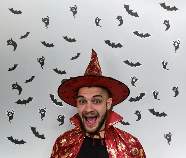 Minimalistic banner celebrating Halloween with bearded Caucasian man in witch costume and black ghosts and bats on white background. Happy Human wearing wizards or magicians hat.