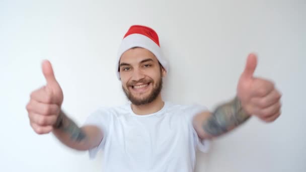 白地に赤いサンタの帽子をかぶった白人ハンサムな男が笑顔で両手でクラスのジェスチャーを作ります クリスマスの喜びと感情 新年を祝う 4K映像 — ストック動画