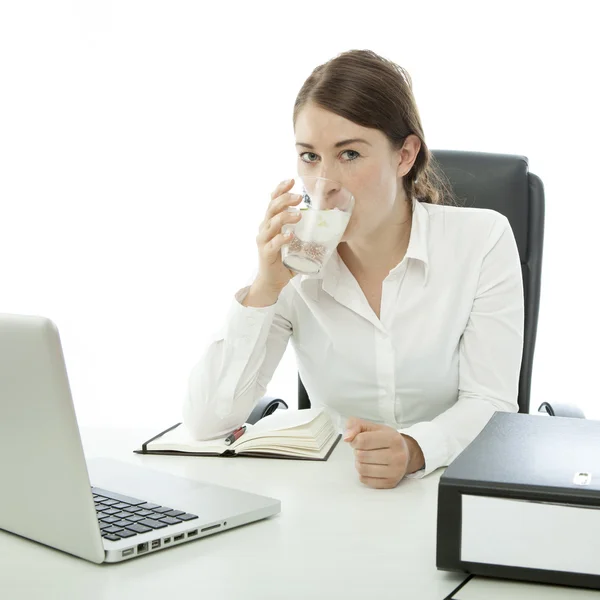 Junge brünette Geschäftsfrau trinkt Wasser vor ihrem Schreibtisch — Stockfoto