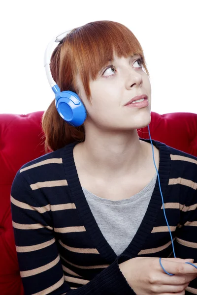 Young beautiful red haired girl on red sofa listen to great musi — Stock Photo, Image