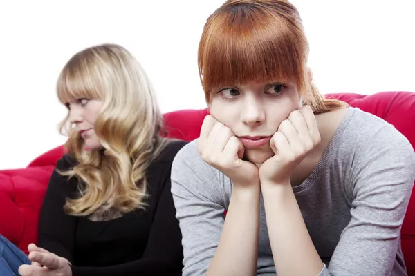 Young beautiful blond and red haired girls sitting on red sofa a — Stock Photo, Image