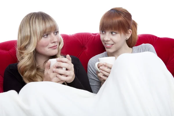 Jonge mooie blonde en rode haired meisjes op rode sofa met coff — Stockfoto