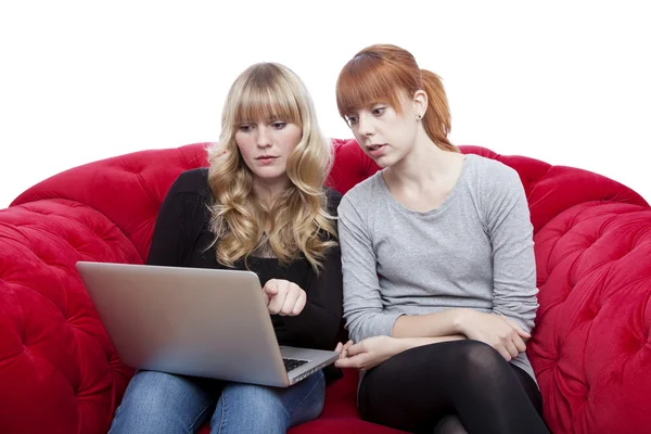Young beautiful blond and red haired girls on red sofashowing so — Stock Photo, Image