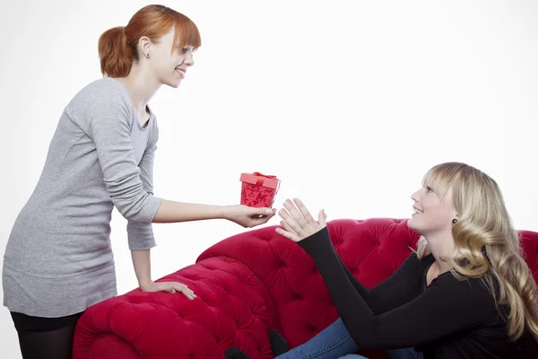 Young beautiful blond and red haired girls on red sofa have a pr — Stock Photo, Image