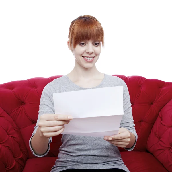 Young beautiful red haired girl on red sofa reading a letter in — Stock Photo, Image