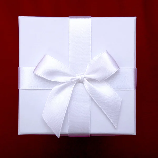Beautiful white gift box with ribbon on top of red sofa backgrou — Stock Photo, Image