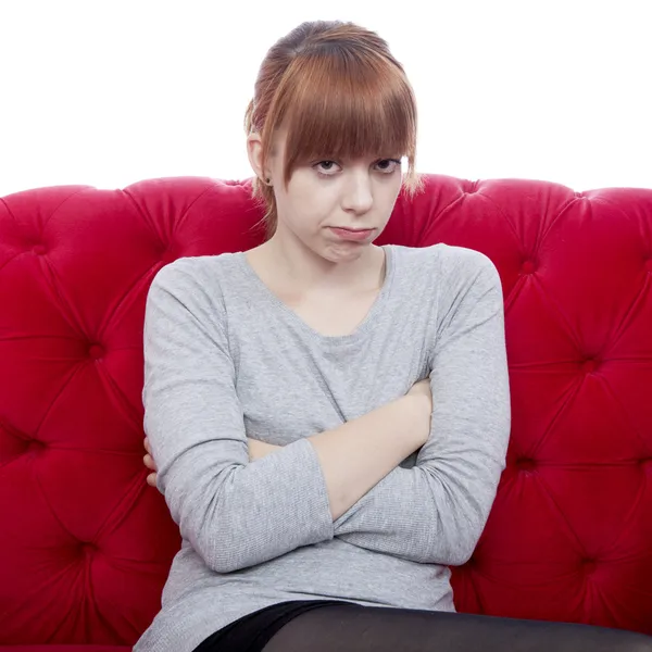 Young beautiful red haired girl on red sofa is offended in front — Stock Photo, Image