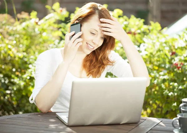 Lachende vrouw die zit in de tuin met behulp van een mobiele — Stockfoto