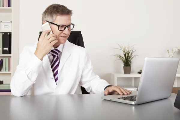 Médico usando telefone celular e laptop — Fotografia de Stock