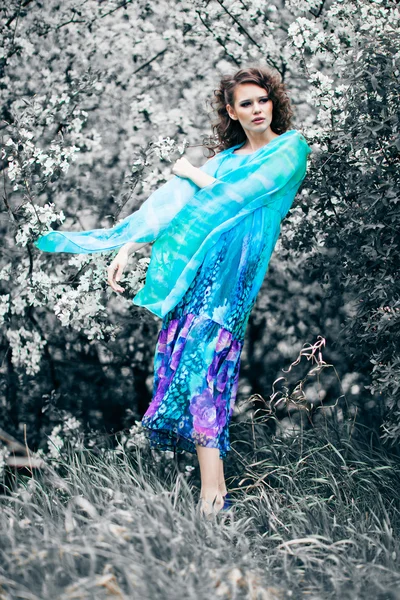 Krásná žena v modrých šatech mezi květ jabloně, móda — Stock fotografie