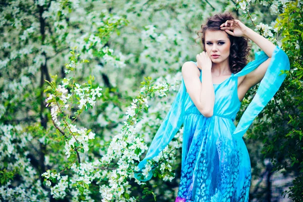 Vacker kvinna i blå klänning bland blossom äppelträd, mode — Stockfoto